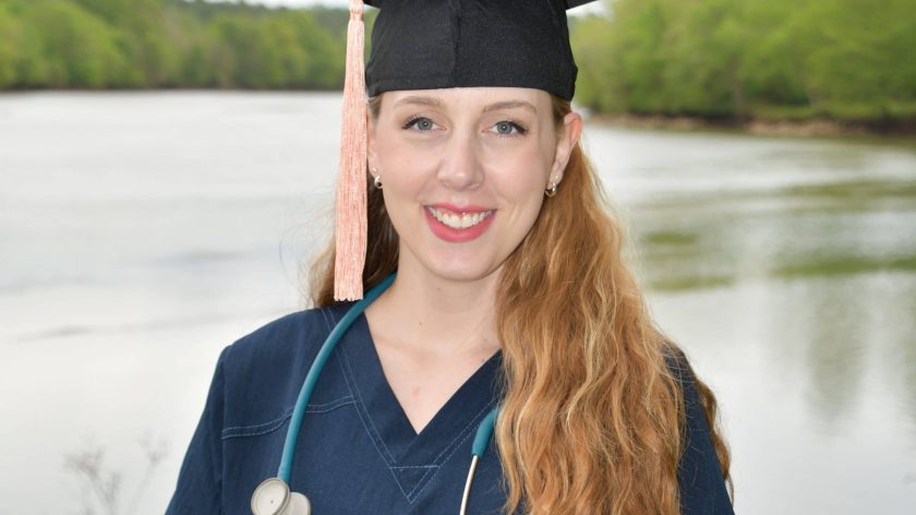 A Woman Wearing A Hat Standing In Front Of A Body Of Water