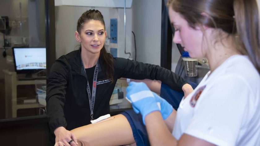 Nursing Students Work With A Mannequin In A Lab Setting.