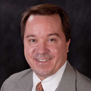 A Man Wearing A Suit And Tie Smiling At The Camera
