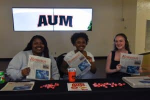 Three members of The Aumnibus staff display copies of their first print issue since 2018.