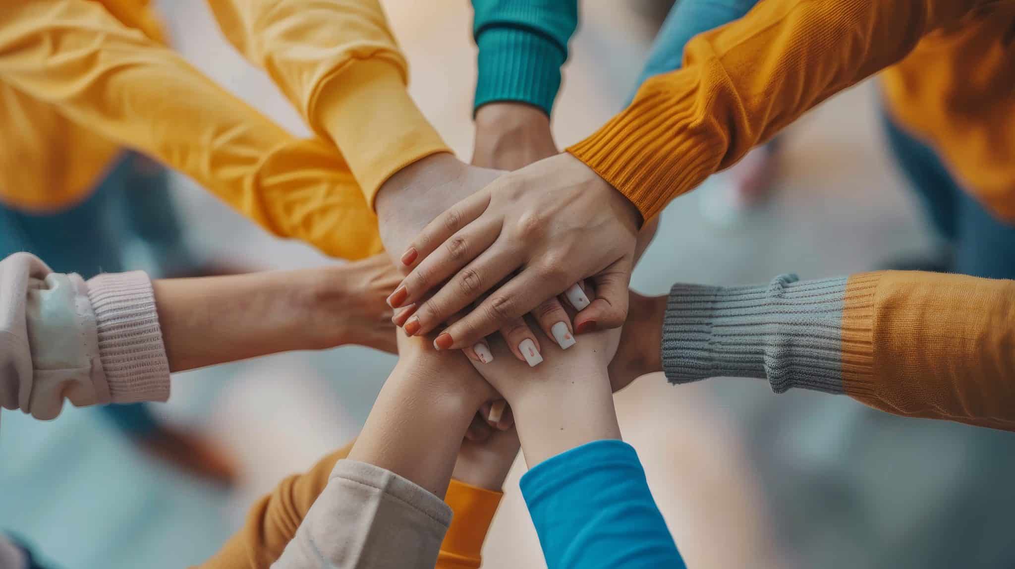 Hands of diverse people stacked together symbolizing teamwork and unity in colorful sweaters.