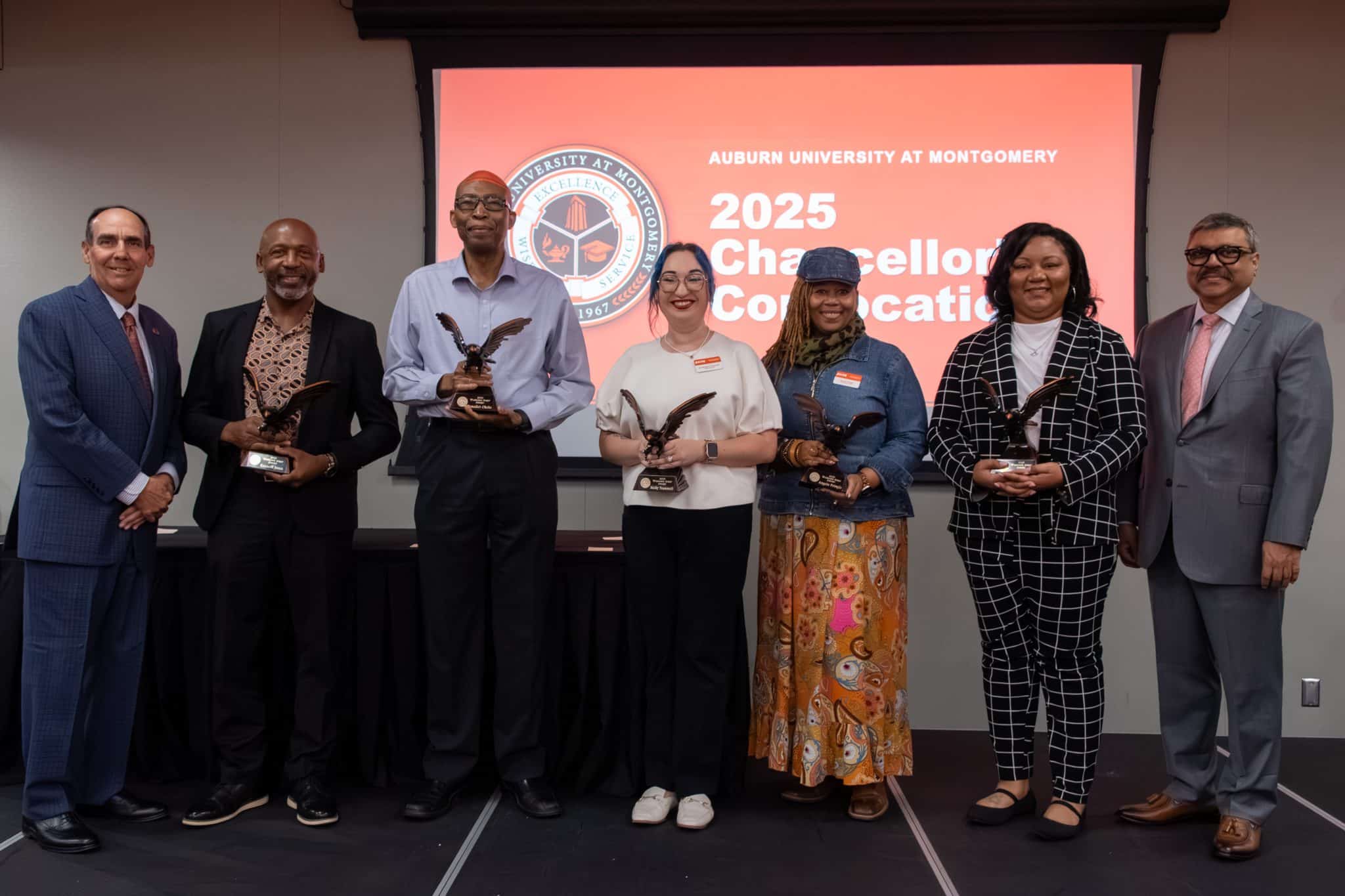 Auburn University at Montgomery 2025 Chancellor's Convocation awardees holding eagle statues on stage.