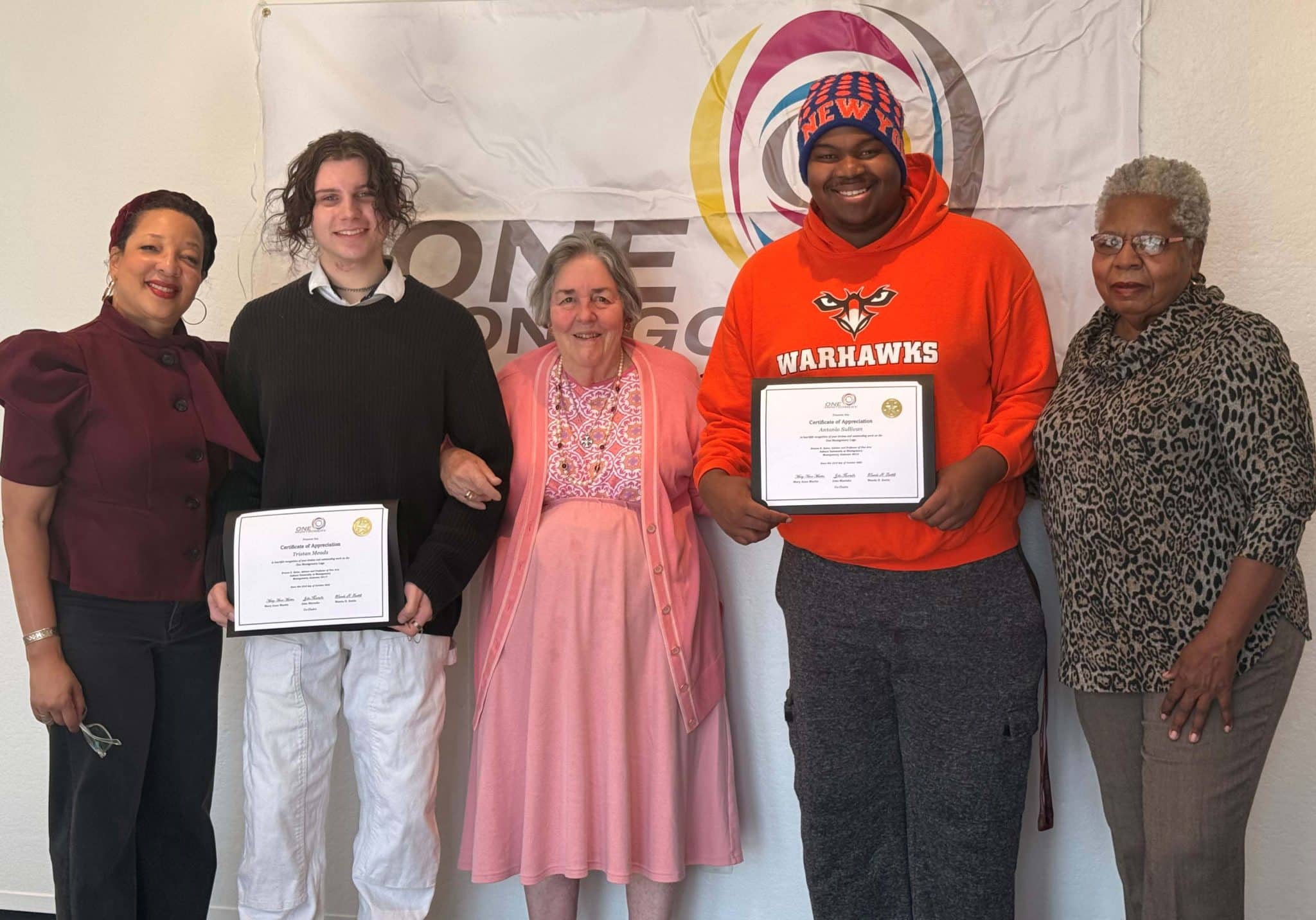 A group of people, two holding certificates, stand in front of a banner for Auburn University at Montgomery.