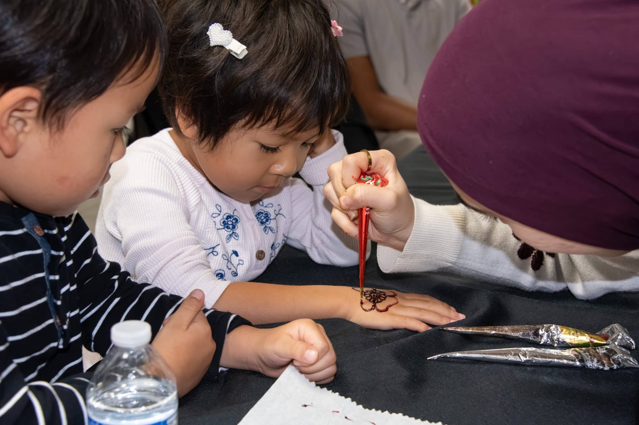Child receives intricate henna design on hand during cultural event at Auburn University at Montgomery.
