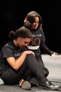 Two Students Perform On Stage Wearing Theatre AUM 50th Anniversary Shirts.