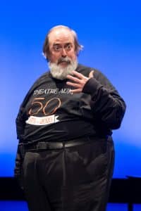Man In Black Shirt Celebrating 50 Years Of Theatre AUM On Stage With A Blue Background.