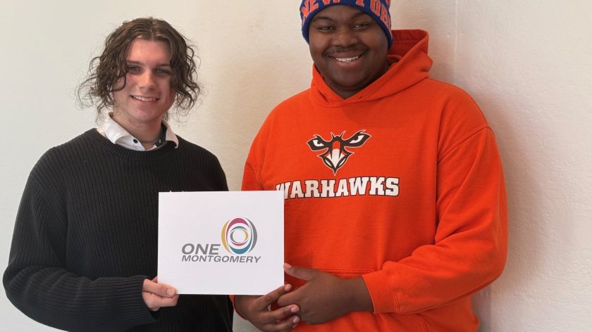 Two People Holding A One Montgomery Sign, One In An Orange Warhawks Hoodie, Auburn University At Montgomery.