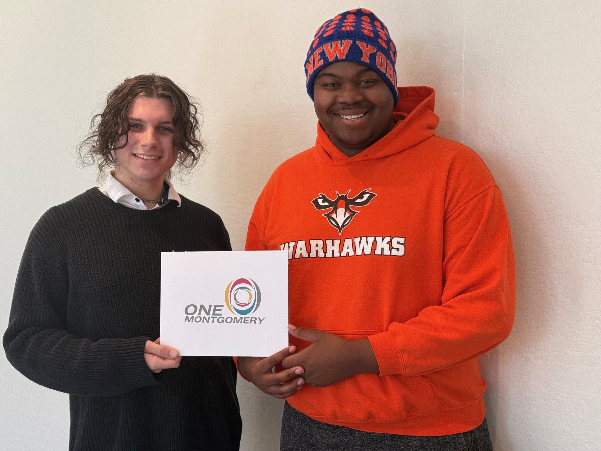 Two people holding a One Montgomery sign, one in an orange Warhawks hoodie, Auburn University at Montgomery.
