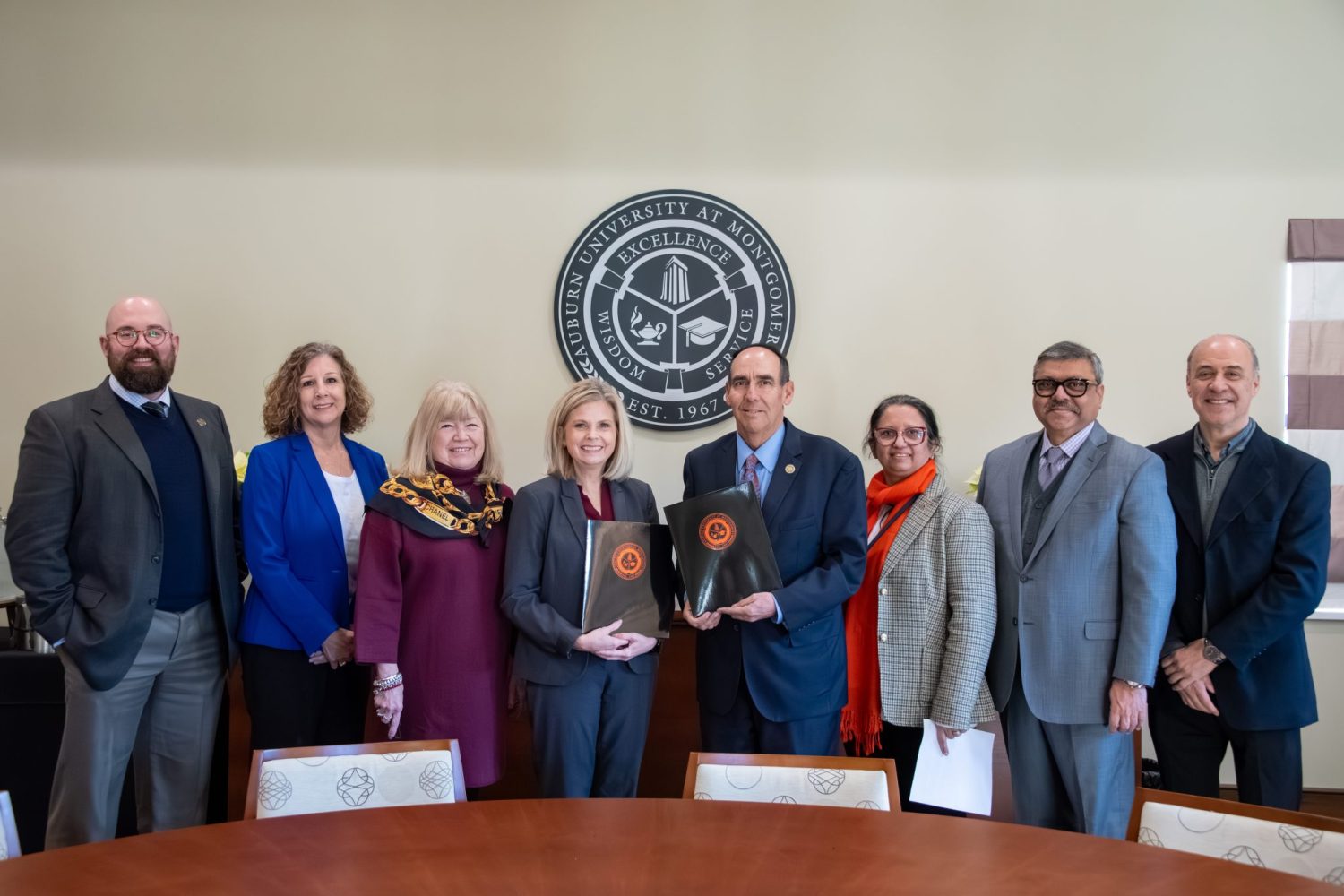 A Group Of People At A Conference Table In Front Of Auburn University At Montgomery Emblem.