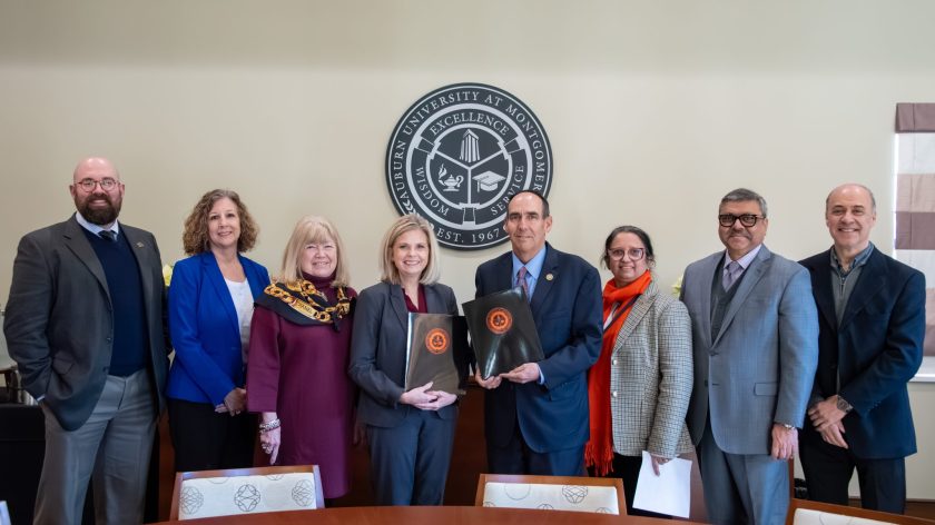 A Group Of People At A Conference Table In Front Of Auburn University At Montgomery Emblem.