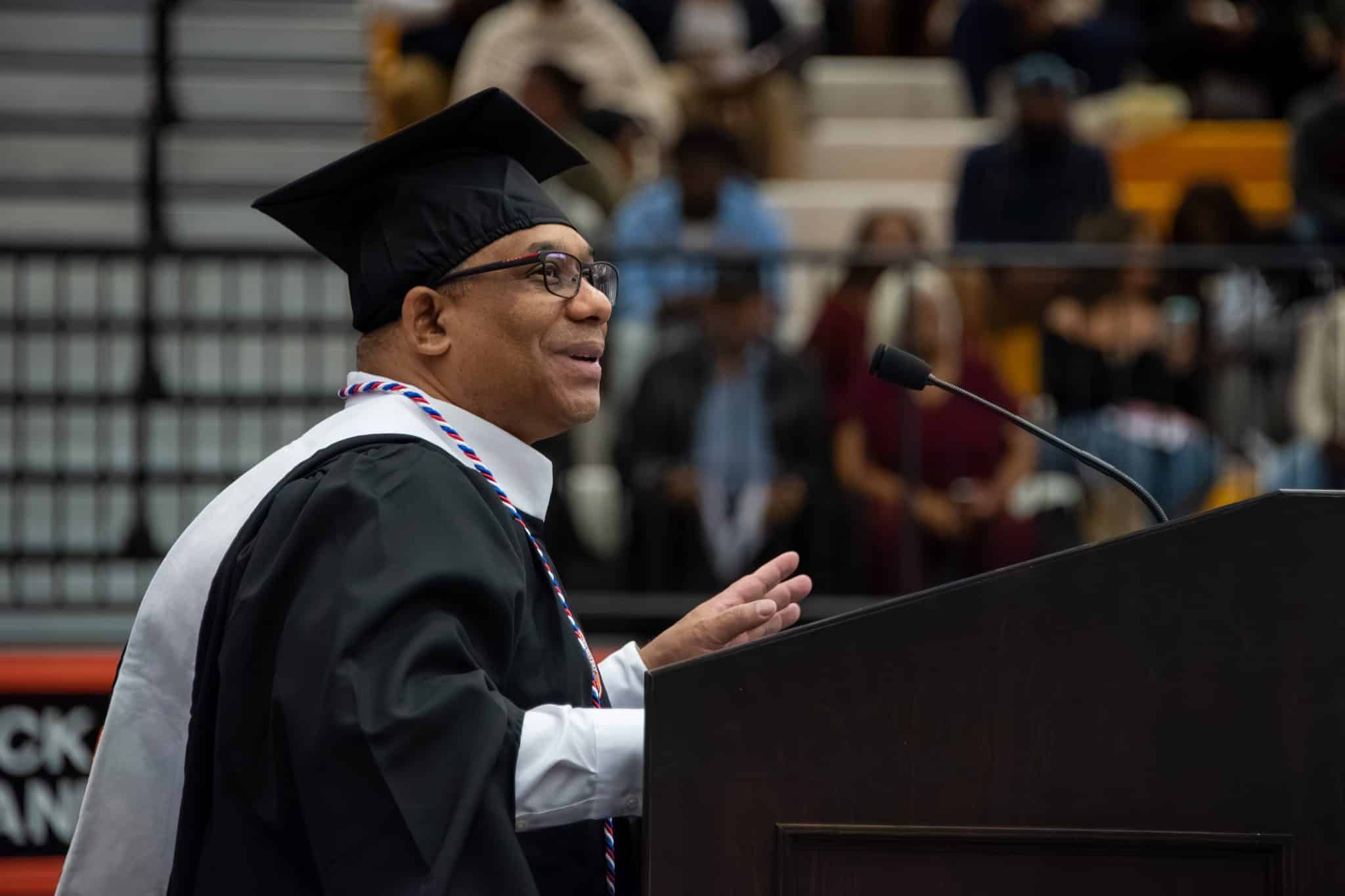 A graduate in cap and gown speaks at a podium during Auburn University at Montgomery's commencement.