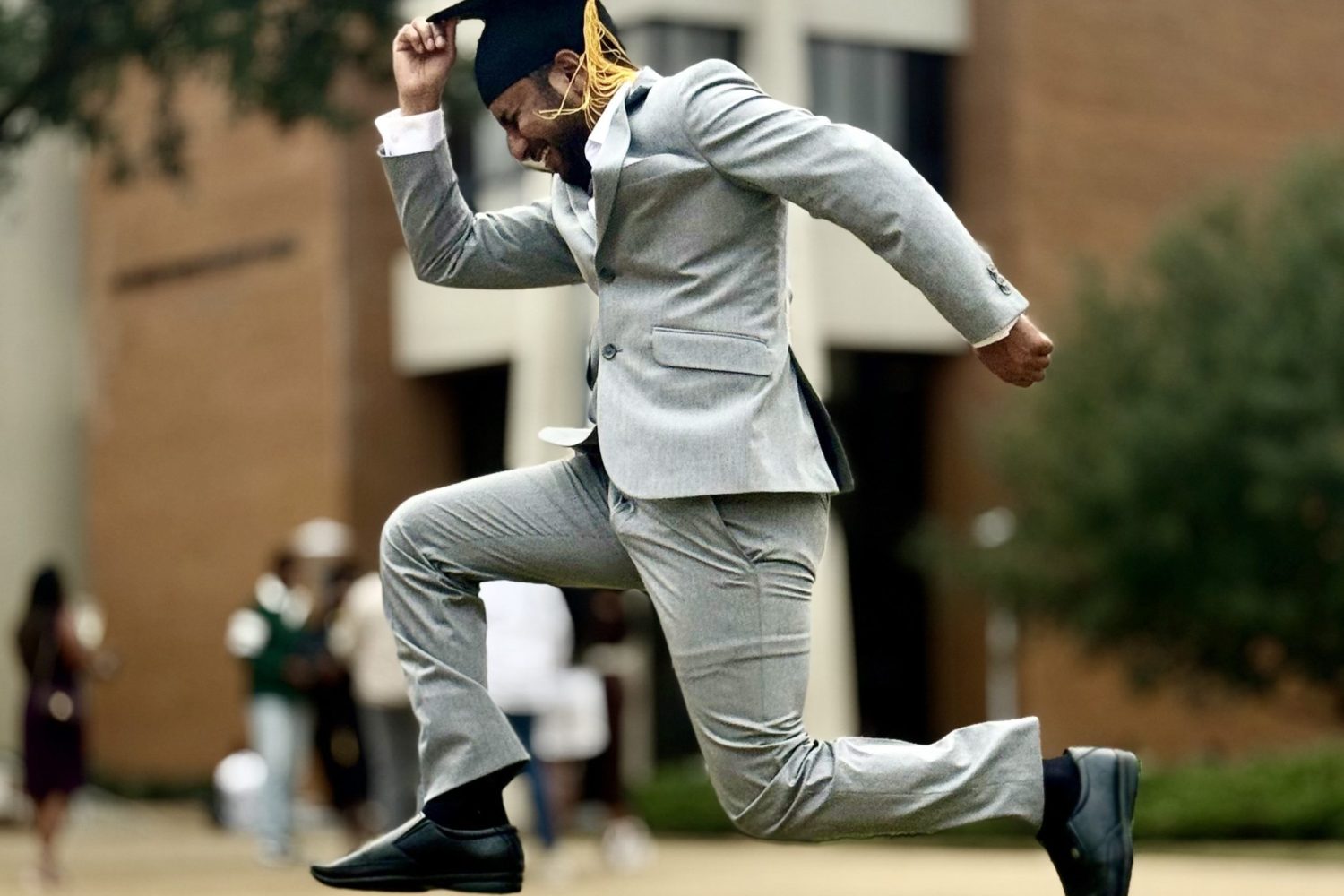 Graduate In Gray Suit Jumps Joyfully With Cap At Auburn University At Montgomery Campus.