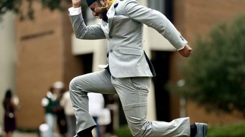 Graduate In Gray Suit Jumps Joyfully With Cap At Auburn University At Montgomery Campus.