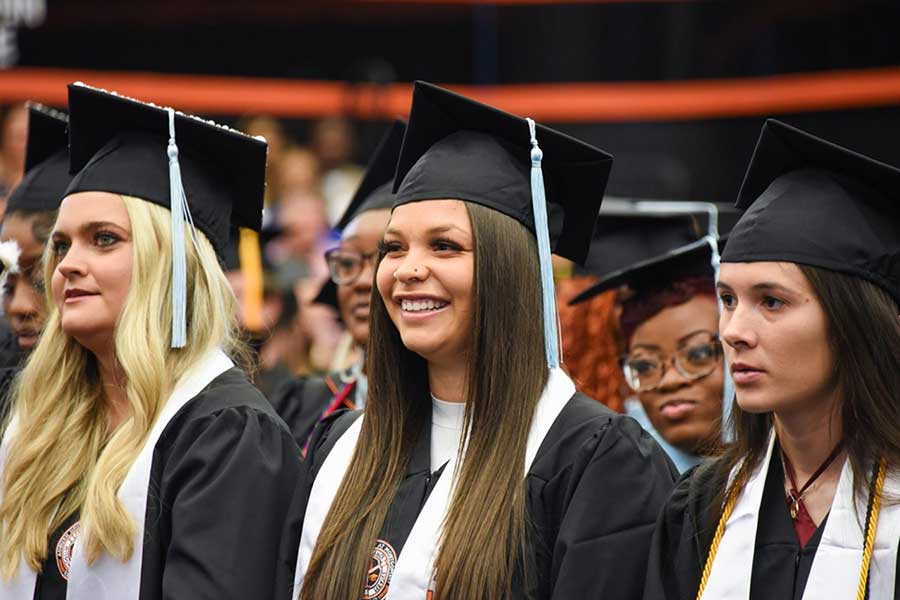 Auburn University at Montgomery graduates in caps and gowns smiling during commencement ceremony.