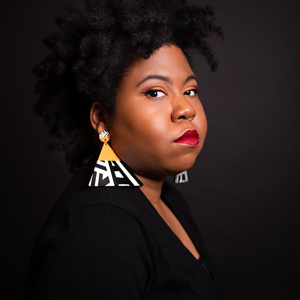 A person poses with colorful geometric earrings against a dark background, showcasing modern artistic style.