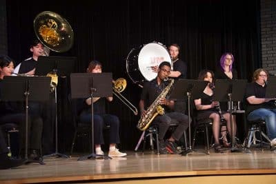 AUM students performing in a band concert on stage with various musical instruments.