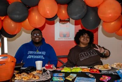 Two students hand out snacks at a table with orange-black balloons at at the Student Resource Fair.