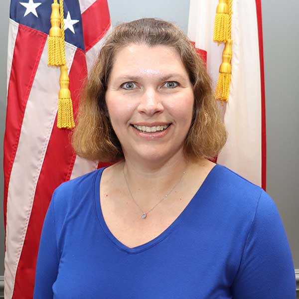 Auburn University at Montgomery staff portrait of a woman in blue, smiling before U.S. and Alabama flags