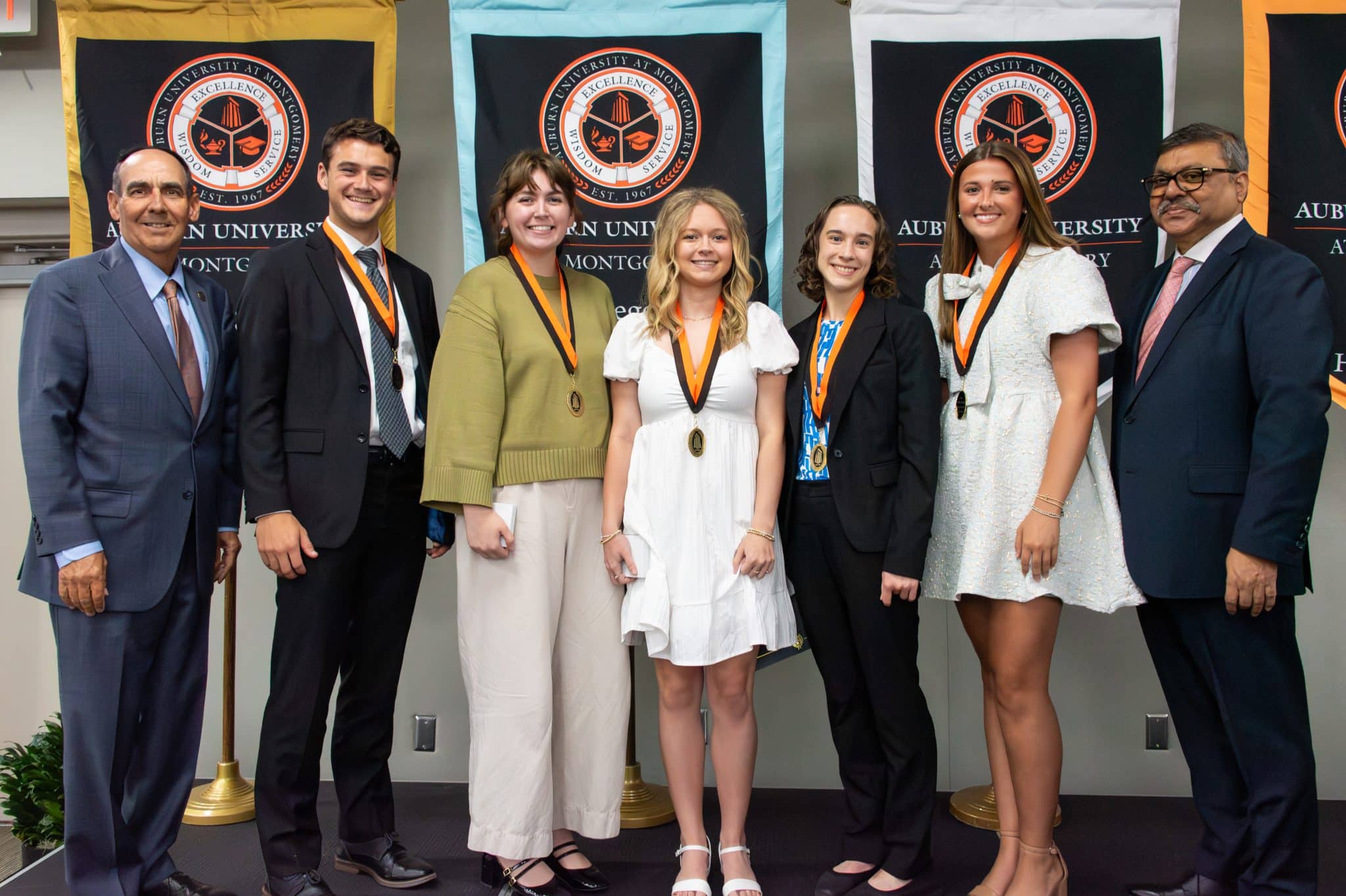 Auburn University at Montgomery honors ceremony: students wearing medals pose with administration before AUM banners.