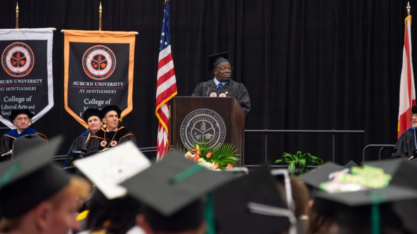 AUM Commencement Speaker At Podium With Auburn University At Montgomery Banners, Addressing Graduates