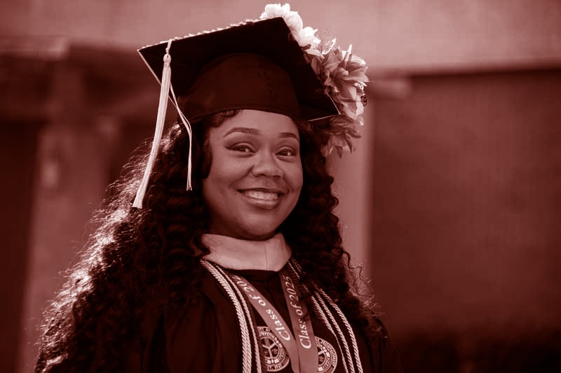 Auburn University at Montgomery graduate smiles in cap and gown at commencement ceremony on campus