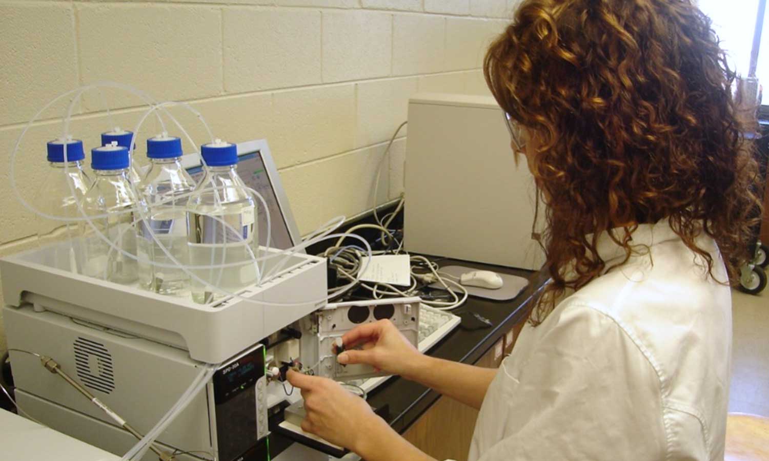 Auburn University at Montgomery lab: a person operates analytical equipment with solvent bottles and computer on a bench