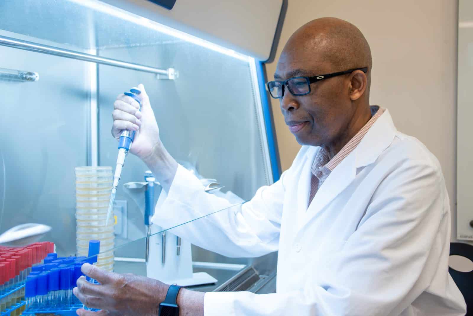 Auburn University at Montgomery researcher using a pipette in a biosafety cabinet, conducting lab tests.